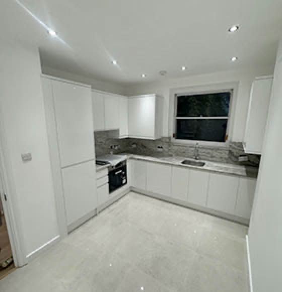 Modern kitchen with white cabinets, marble countertops, an oven, and a window above the sink.