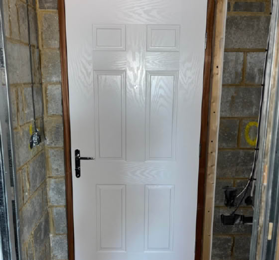 White door with a brown frame set in a brick wall, featuring a black handle on the left side.