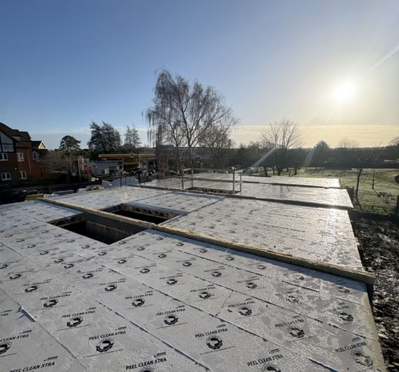 Construction site with a foundation covered in insulation panels, two rectangular openings, and a clear sky with the sun low on the horizon.