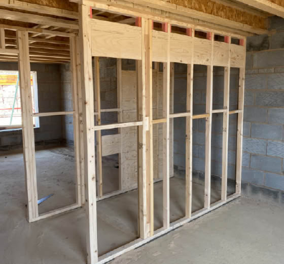 Wooden framing structure inside a building under construction with concrete block walls and an unfinished ceiling.