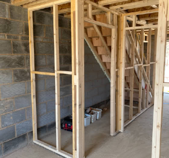 Wooden framing of a staircase under construction, with visible concrete block walls and construction materials on the floor.