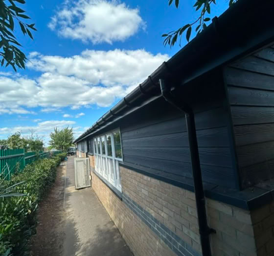Side view of a building with a brick and dark panel exterior, a narrow path alongside, and a blue sky with clouds above.