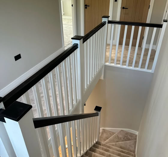 Carpeted staircase with white railings and dark handrails, leading to a hallway with closed wooden doors.
